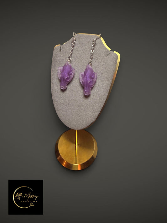 Purple wolf skull dangle earrings on a grey velvet display stand with silver chains.