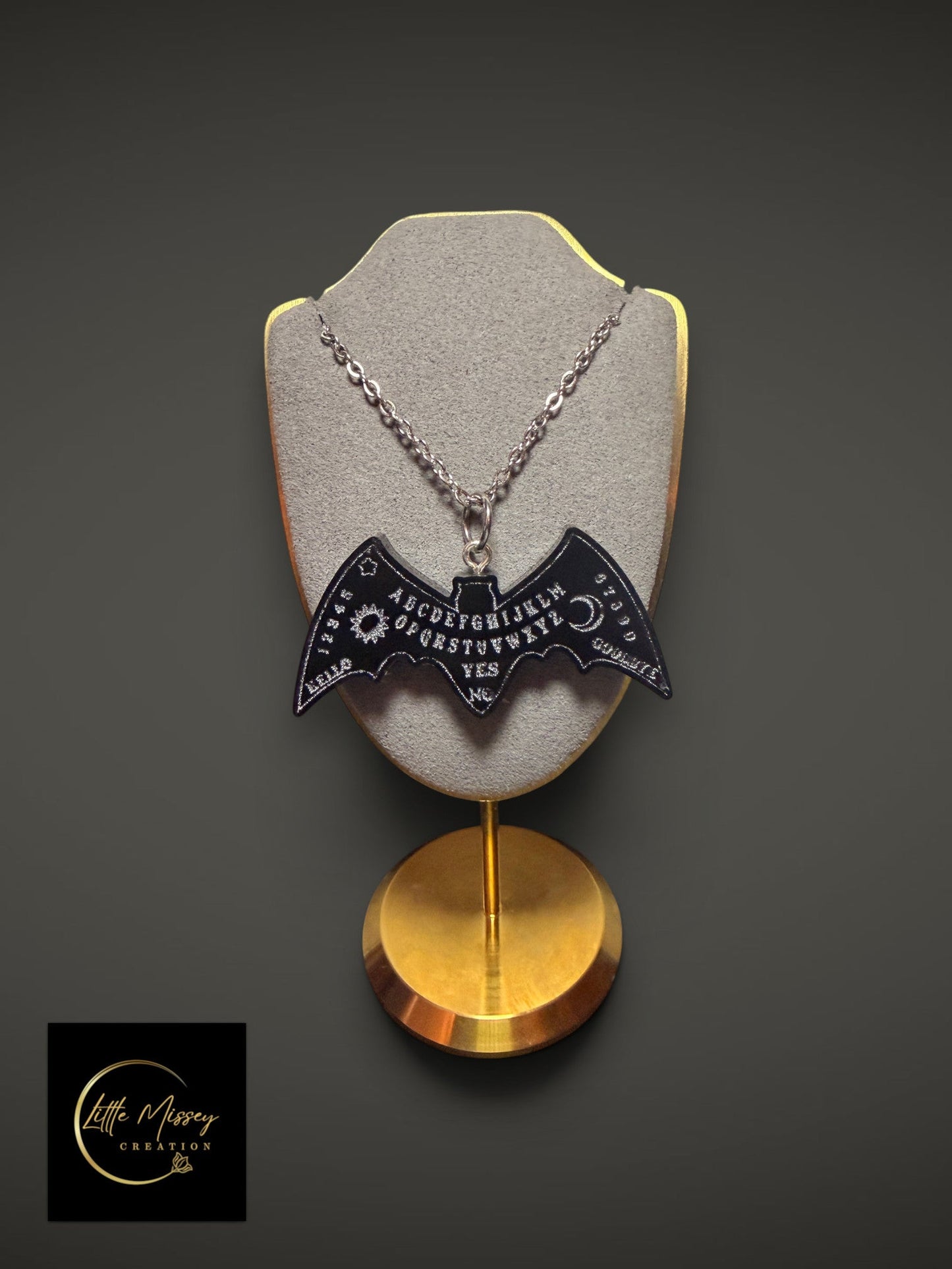 Little Missey Creation black bat-shaped Ouija board pendant necklace on a grey display stand