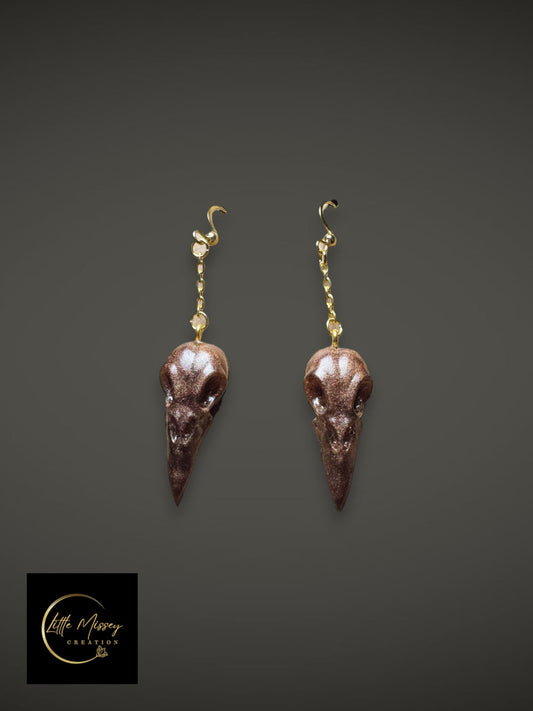 Raven skull earrings in shimmering dark brown resin with gold-toned hardware for gothic style.